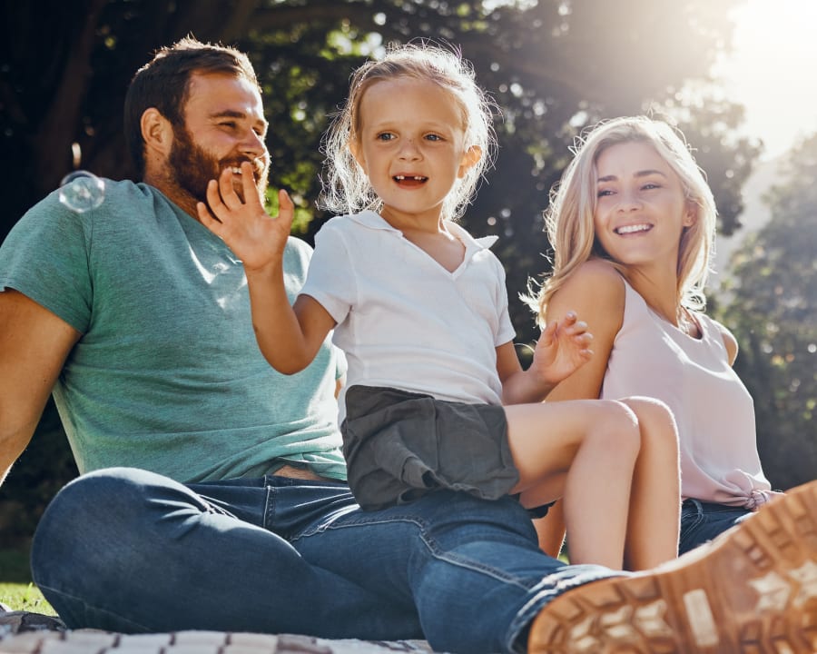A couple is sitting in a park with their young daughter who is missing her two front teeth.
